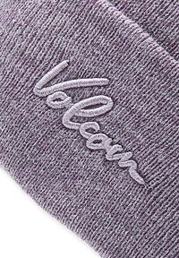 Berretto lavorato a maglia viola con una texture a coste e logo "Volcom" ricamato in bianco. Il tessuto appare morbido e flessibile.