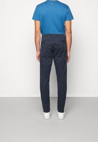 Blå t-shirt och mörkblå byxor, tillverkade av bomull. Byxorna har en rak passform, bakfickor och subtila sömnadsdetaljer. Vita skor.