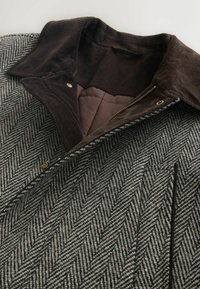 Uz herringbone raksta mēteļa ir brūns korduroja apkakle, zelta detaļas un rāvējslēdzis. Faktūra pelēkā un melnā audumā ar gludu iekšējo oderi.