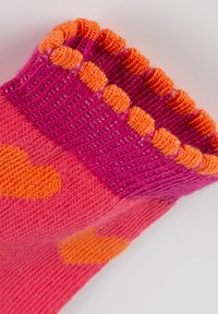 Bunte Socke mit einer Mischung aus rosa und orangefarbenen Nuancen, geripptem oberen Rand mit Pompon-artigem Besatz und Herzmustern in Orange auf einem rosa Hintergrund.