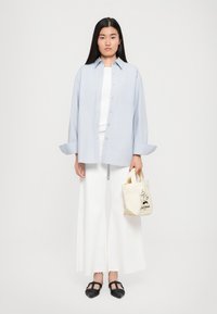 Lyseblå oversized knappopp skjorte, hvit tettsittende topp, luftige hvite vide bukser, svarte vevde sko og en liten beige tote-veske med grafikk.