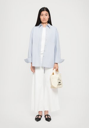 Lyseblå oversized knappopp skjorte, hvit tettsittende topp, luftige hvite vide bukser, svarte vevde sko og en liten beige tote-veske med grafikk.