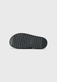 Black rubber shoe sole featuring horizontal grooves for grip, a slight curve at the toe, and a branded label near the center.