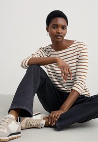 Gestreepte lange mouwen top in crème en bruin, gecombineerd met zwarte wijde broek en beige sneakers. Eenvoudig ontwerp, zachte textuur, ontspannen pasvorm.