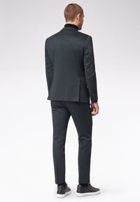 Ciemnoszary garnitur o dopasowanej sylwetce, teksturowanej tkaninie, z jednym rozcięciem, i czarnym golfem. Stylizowany z czarnymi sneakersami.