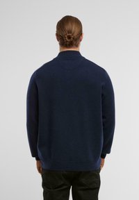 Dunkelblauer Pullover mit hohem Kragen, weicher Textur, lockerer Passform und gerippten Bündchen. Verfügt über einen glatten Rücken und ein minimalistisches Design.