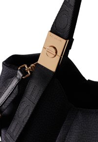 Schwarze Handtasche aus strukturiertem Stoff, mit einem breiten Tragegurt, der geprägte Schriftzüge aufweist, und einem Verschluss aus goldfarbigem Metall.