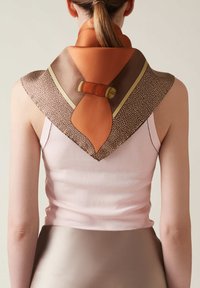 Foulard di seta con un design arancione e marrone. Presenta una forma a V con un dettaglio a nodo e texture contrastanti. Indossato attorno al collo.