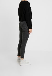 Svart stickad kort tröja, grå leopardmönstrade smala jeans, vita högre sneakers. Sidovy som framhäver passform och textur.