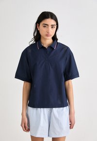 Polo shirt navy con maniche corte, dotato di patta con bottoni e colletto a righe rosse e bianche; dettaglio in rete sui lati.