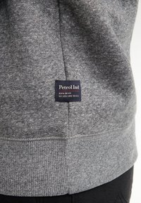 Grijze sweatshirt met een zachte, gestructureerde afwerking. Bevat een donkerblauw etiket met de tekst "Petrol Ind" in wit en rood op de onderzoom.