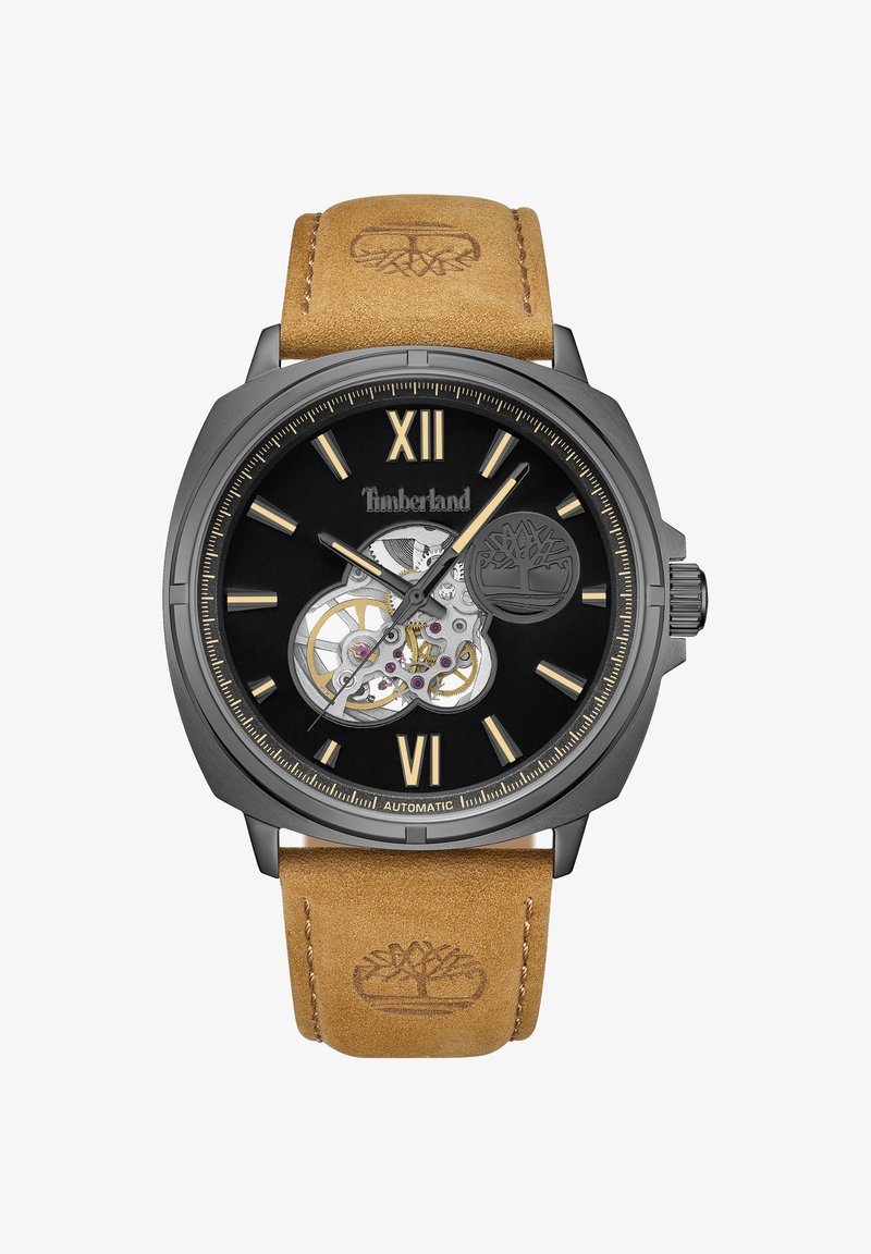 Montre automatique noire avec index dorés, cadran squelette transparent et bracelet en cuir marron embossé du logo.