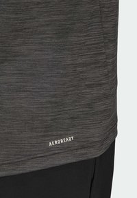 T-shirt de sport gris avec un tissu texturé qui évacue l'humidité, présentant un motif subtil et un logo blanc "AEROREADY" à l'ourlet.