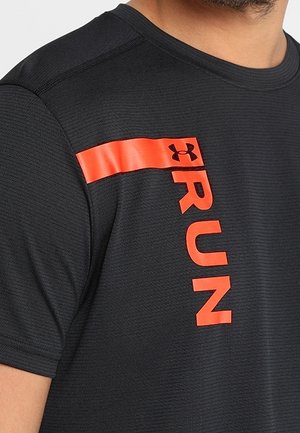 Mężczyzna w czarnej teksturowanej koszulce z krótkim rękawem z czerwoną linią i pionowym czerwonym tekstem "RUN" z logo Under Armour na piersi.