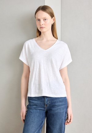 T-shirt blanc à col en V avec des manches courtes, en tissu léger, porté avec un jean en denim bleu. Design simple et minimaliste avec une coupe décontractée.