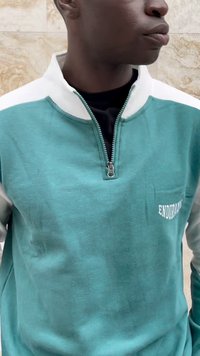 Tyrkis og hvit zip-up hettegenser med høy krage, med en frontlomme og "ENDURANCE" tekst i hvitt på venstre side. Myk tekstur.
