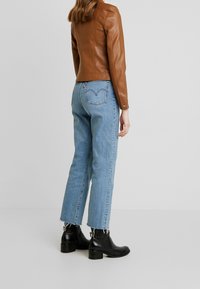 Brun læderjakke med tætsiddende design, kombineret med lyseblå jeans med lige ben. Sorte ankelstøvler med blokhæl og frynse detaljer.