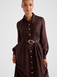 Pruun nööbitav kleit pikkade varrukatega, vöökohal vööga, kuldse tooniga nööpidega ja siledat tekstuuri omav. Omab klassikalist kraed ja lõdvestunud istuvust.