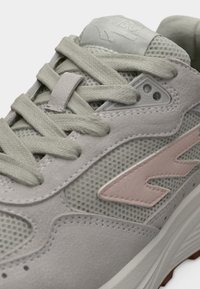 Lichtgrijze sneaker met een mix van mesh- en suède materialen. Voorzien van platte veters, een roze accent en een gestructureerde rubberen buitenzool.