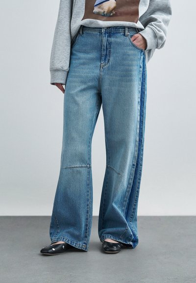 Ljusblå jeans med vida ben och en mörkare blå sidopanel, gjorda av bomullstyg, klassisk design med fem fickor och lätt blekning på benen.