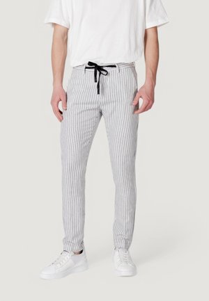 Pantaloni a strisce bianchi e grigi con vita regolabile e vestibilità affusolata, abbinati a sneaker bianche. Tessuto leggero con una texture liscia.