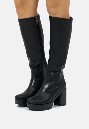 Schwarze kniefreie Stiefel mit glänzender, synthetischer Oberfläche, seitlichem Reißverschluss, auffälligem Blockabsatz und abgerundeter Spitze. Glatte Textur mit minimalen Details.