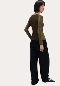 Top metálico dorado de manga larga con un diseño ajustado, combinado con pantalones anchos negros con puños abotonados y zapatos planos negros de punta.