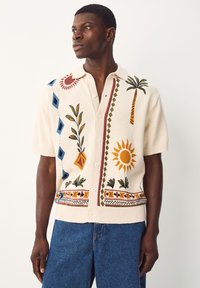 Kortærmet cream strikskjorte med farverige broderede mønstre af blomster, sol og palmer, med klassisk krave og knaplukning.