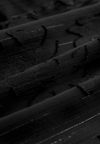 Czarna tkanina o warstwowych fakturach, z lekko błyszczącą powierzchnią i wypukłymi wzorami kwiatowymi. Gładka, z subtelnymi poziomymi paskami.