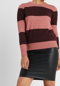 Sweter w paski z naprzemiennymi odcieniami różu i ciemnego burgundu, wykonany z miękkiego materiału z prążkowanymi mankietami i dolnym brzegiem. Zestawiony z czarną skórzaną spódnicą.