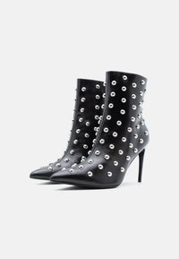 Čierne kožené členkové čižmy so striebornými cvokmi, špicatou špičkou a ihlovým podpätkom. Majú hladkú štruktúru a priliehavý strih.