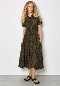 Grünes und schwarzes Zebra-Print Hemdkleid mit kurzen Ärmeln, tailliertem Bund, seitlichen Taschen und fließendem Schnitt. Tragen mit schwarzen Sandalen.