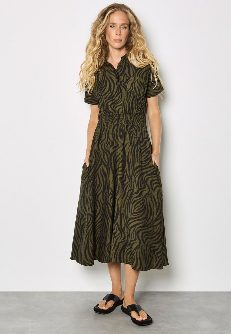 Grünes und schwarzes Zebra-Print Hemdkleid mit kurzen Ärmeln, tailliertem Bund, seitlichen Taschen und fließendem Schnitt. Tragen mit schwarzen Sandalen.