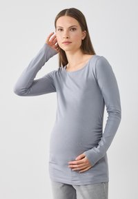 Hosszú ujjú, szürke kismama blúz puha anyagból, kerek nyakkivágással és testhezálló fazonnal, a csípő alatt érkező, kényelmes viselet.