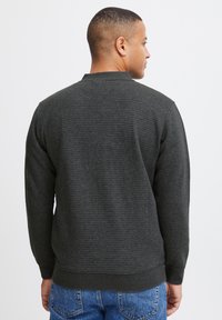 Sudadera texturizada de color gris oscuro con puños y dobladillo acanalados, con cuello redondo y un ajuste relajado, combinada con jeans azules.