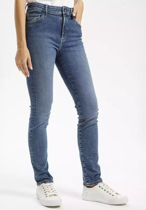 Jeansy z wysokim stanem w niebieskim kolorze, o slim fit, z przednimi kieszeniami i subtelnymi detalami w szwie, połączone z białymi sneakersami.