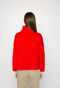 Czerwony, pluszowy polar z wysokim kołnierzem, opadającymi ramionami i luźnym krojem. Gładka tekstura z prostym, jednolitym wzorem.