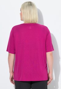 Camiseta de manga corta magenta, con cuello redondo, fabricada en un tejido suave y con una textura lisa; presenta un logo sutil cerca del cuello en la parte de atrás.