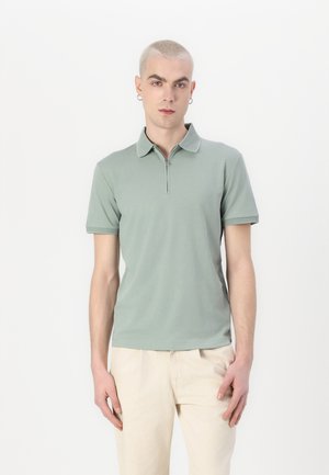Polo shirt verde chiaro con colletto con zip e maniche corte. Tessuto di cotone liscio con una trama a contrasto sul colletto.