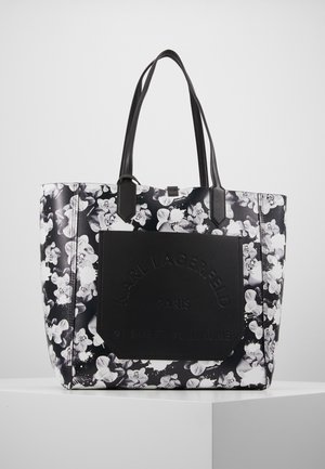 Black and white floral tote bag with dual long handles and a large black front pocket embossed with "Karl Lagerfeld Paris" text.