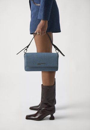 Blue denim clutch bag with a flat design, featuring a black handle, and logo detailing. Worn with brown high-heeled boots.