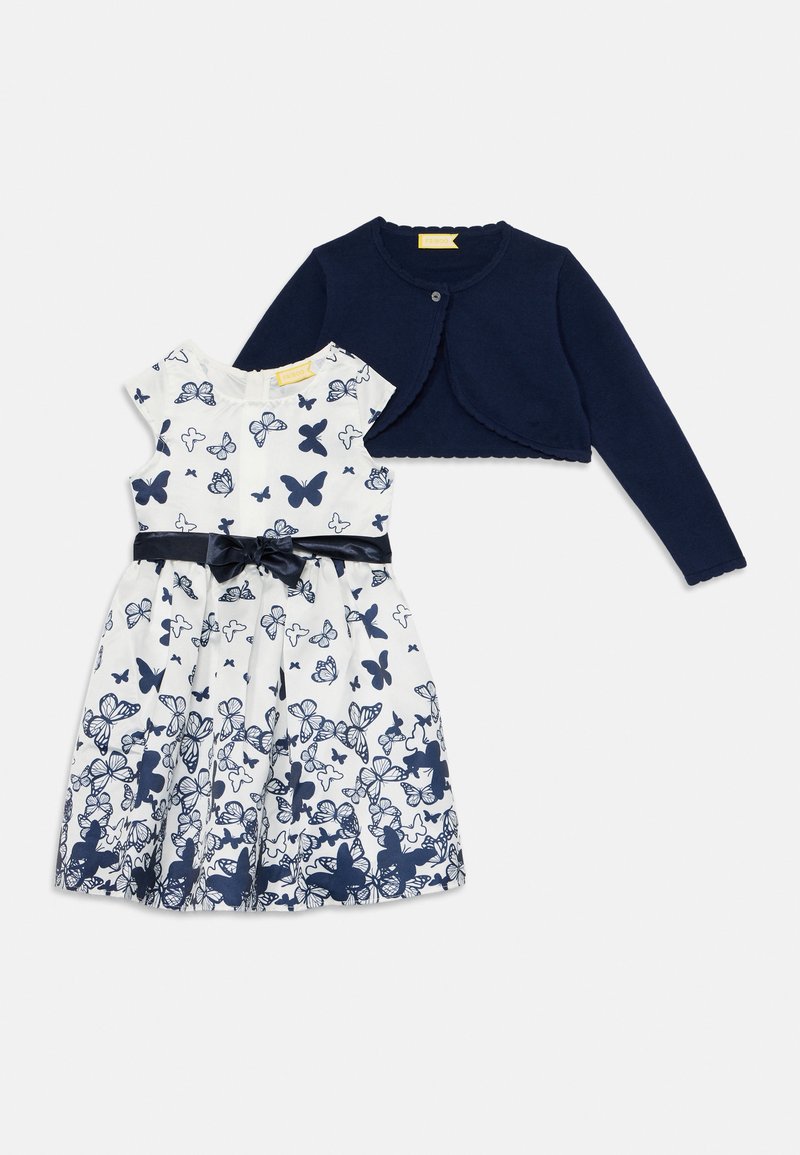 Cardigan blu navy con bordi ondulati abbinato a un vestito bianco con motivo a farfalla blu e un nastro navy in vita.