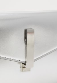 Borsa a mano metallizzata argentata con un design elegante, caratterizzata da una finitura lucida e una chiusura rettangolare argentata. I bordi cuciti aggiungono dettaglio.