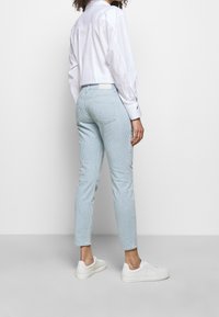Light blue, striped trousers with a slim fit, made from woven fabric. Styled with a white, collared shirt and white sneakers.
