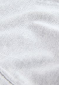 Nahaufnahme einer weichen weißen Stoffstruktur mit sichtbarem Strickmuster und dezenten Falten.