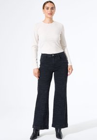 Zwarte jeans met zebraprint en wijde pijpen, gemaakt van denim, gecombineerd met een aansluitend lichtbeige langemouwen shirt en zwarte haklaarzen.