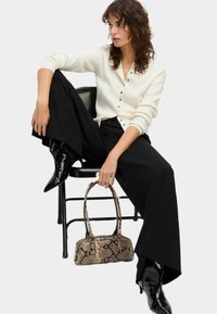 Cardigan bianco a coste con bottoni, pantaloni neri a gamba larga, stivaletti neri con punta e una borsa in pelle di serpente texturizzata.