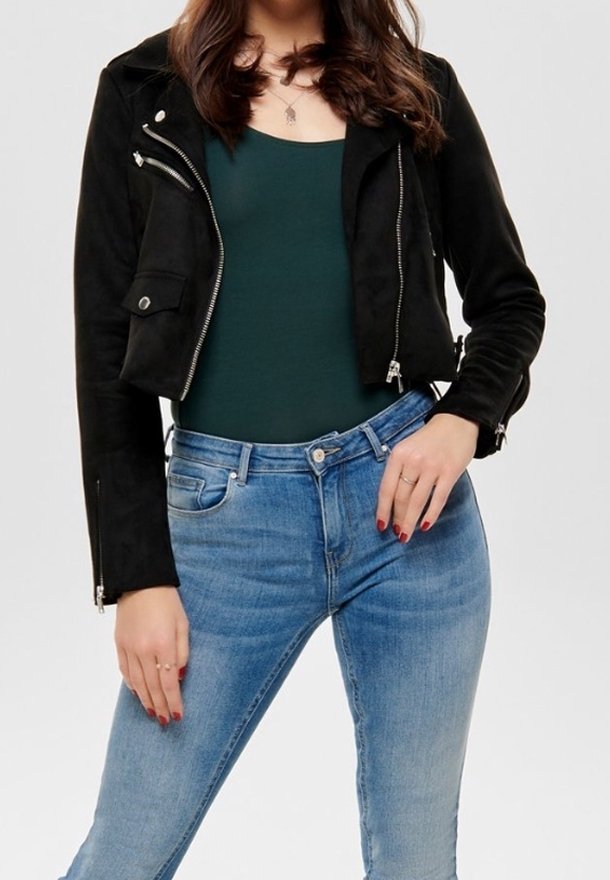 Zwarte suède cropped jas met rits- en zakdetails, gecombineerd met aansluitende blauwe denim jeans en een donkergroene top.