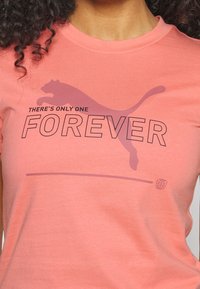 Růžové bavlněné tričko s krátkým rukávem, které má velký tmavý grafický text "FOREVER" a siluetu pumy.