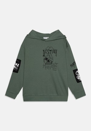 Zelena kapuca z njeno grafiko spredaj, na kateri je besedilo, dizajn lobanje in strela. Črna nalepka z lobanjo na vsaki rokavu. Mehka tkanina, sproščen kroj.